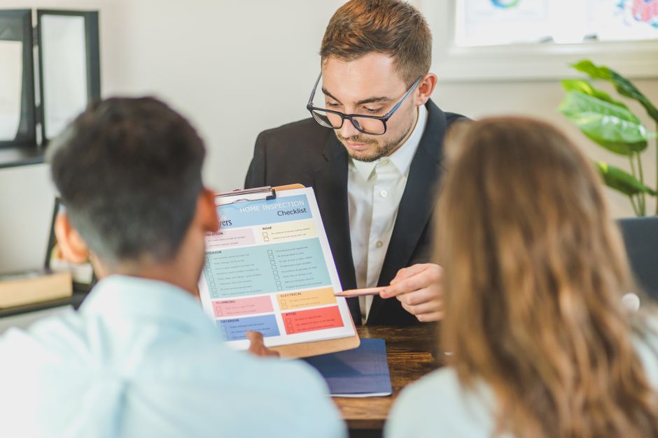 Real estate agent explaining home inspection checklist to clients in an office setting.