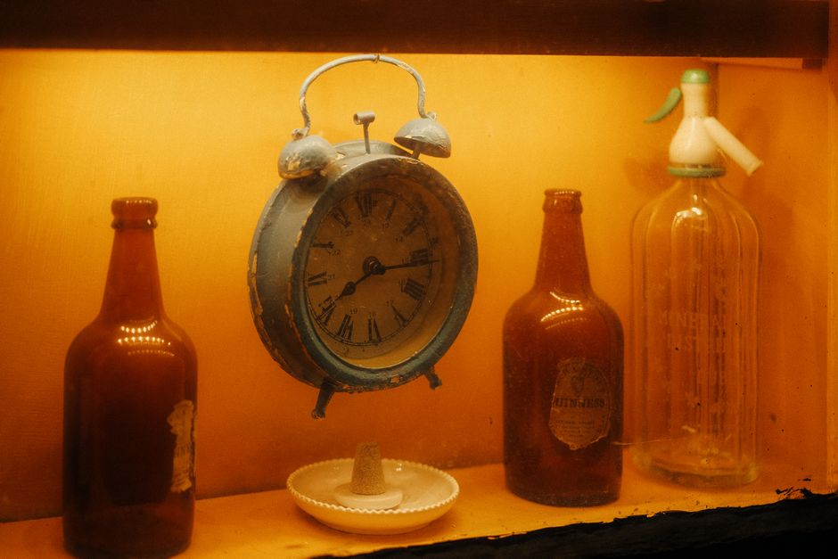 A warm, vintage display featuring a rustic alarm clock surrounded by antique bottles.