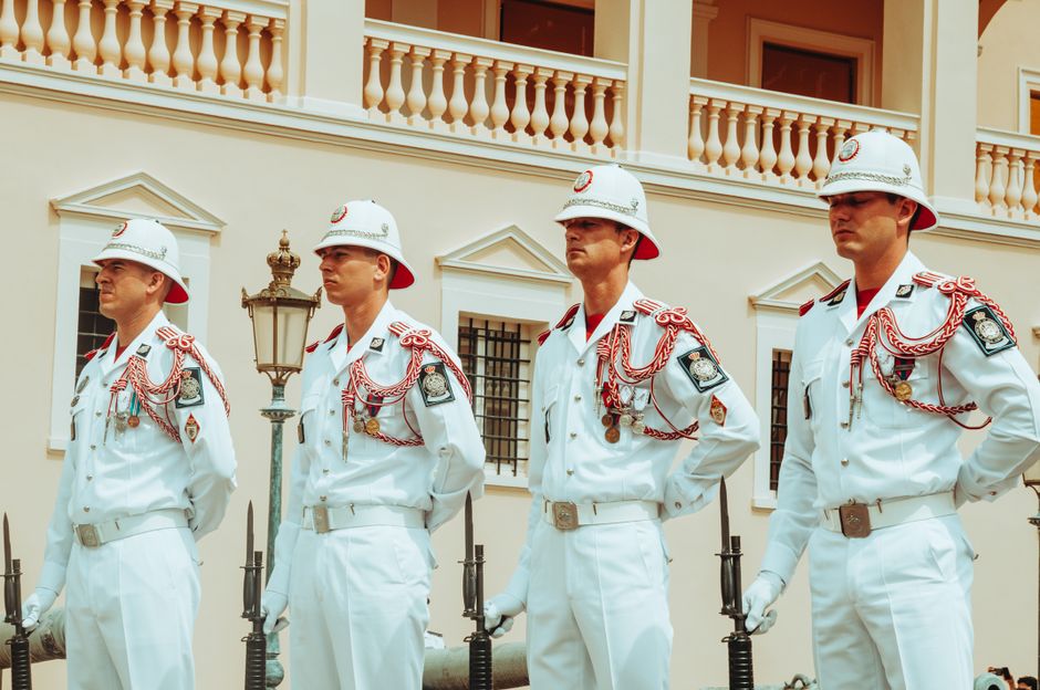 Four uniformed guards in white attire stand in formation outside a classical building.